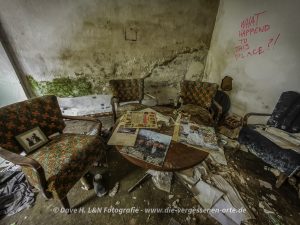 In einem dunklen Zimmer der Indudtrieruine steht ein Tisch. Wände verwaisten Ortes sind mit Schimmel überzogen.