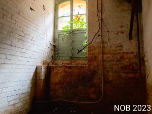 Ein großes Fenster in einem dunklen Raum, die Rahmen sind überzogen von Rost.