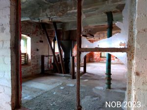 Durch ein Loch einer zerbrochenen Scheibe der Ölmühle sieht man noch ein paar alte Maschinen an denen der Rost sich langsam breit macht.