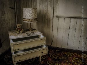 Auf Lost Place Tour: In einem Zimmer eines verlassenen Hotels befindet sich nein Nachttisch mit einer urigen Lampe drauf.