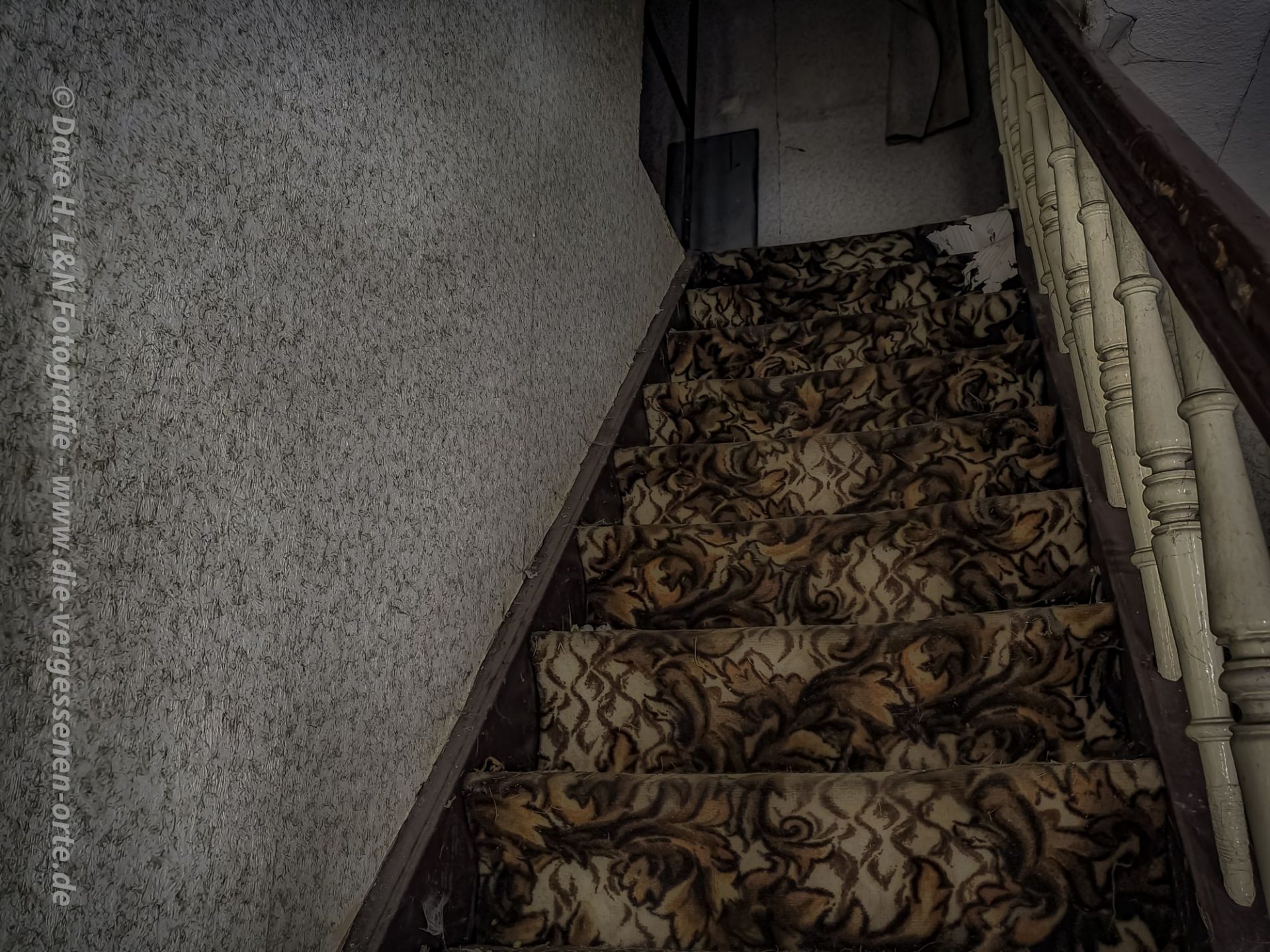 Eine Treppe, ausgelegt mit altem Teppich, führt hinauf zu den Zimmern dieser verlassenen Pension.