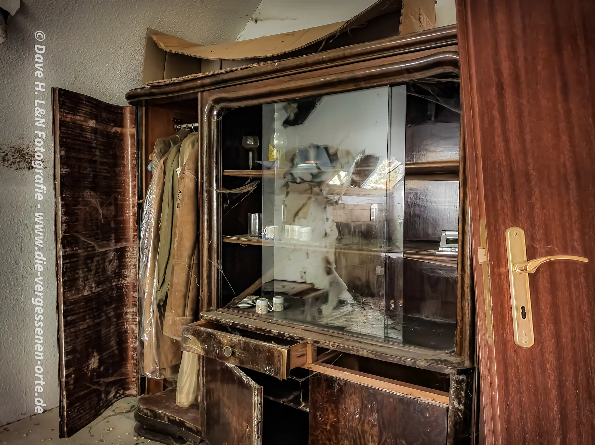 Alte Vitrine mit raushängenden Türen im verlassenen Wohnhaus.