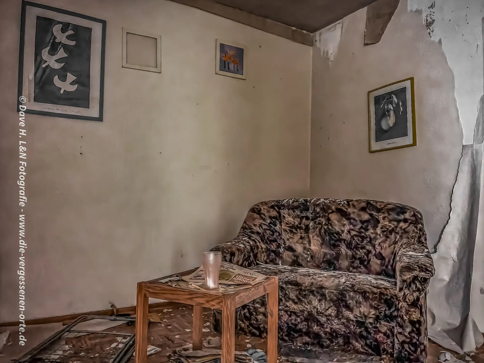 Couch und Wandbilder in der ehemaligen Ferienunterkunft – ein verlassener Ort mit Wohngefühl.