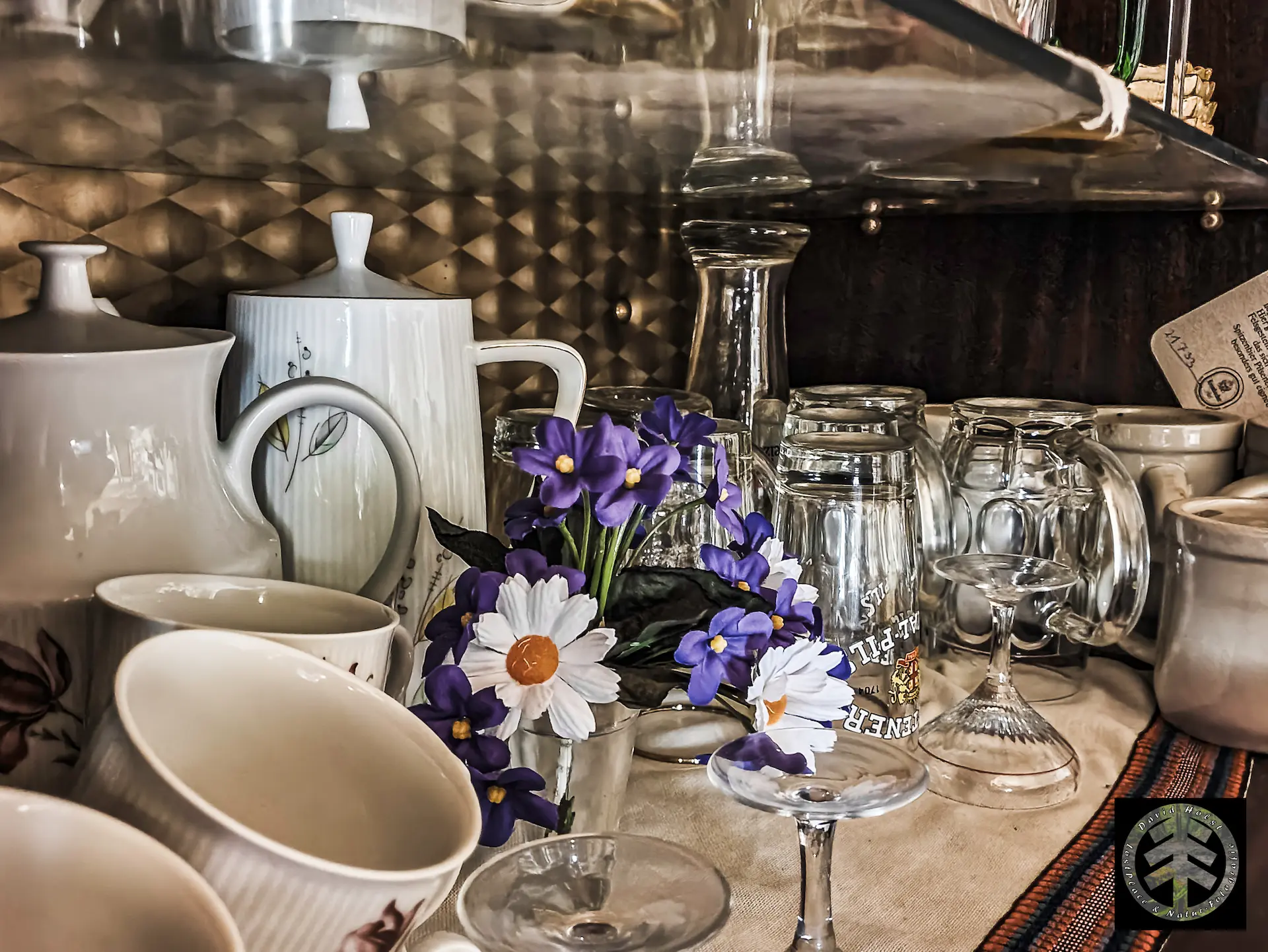 Gläser und Plastik-Blumen im Schrank einer Vitrine.