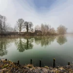 Verlassenes Wochenendhaus mit See im Vordergrund in idyllischer Atmosphäre